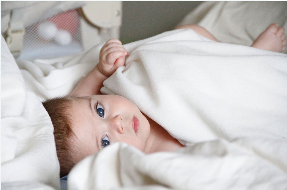 A baby peeking out from under a white blanket